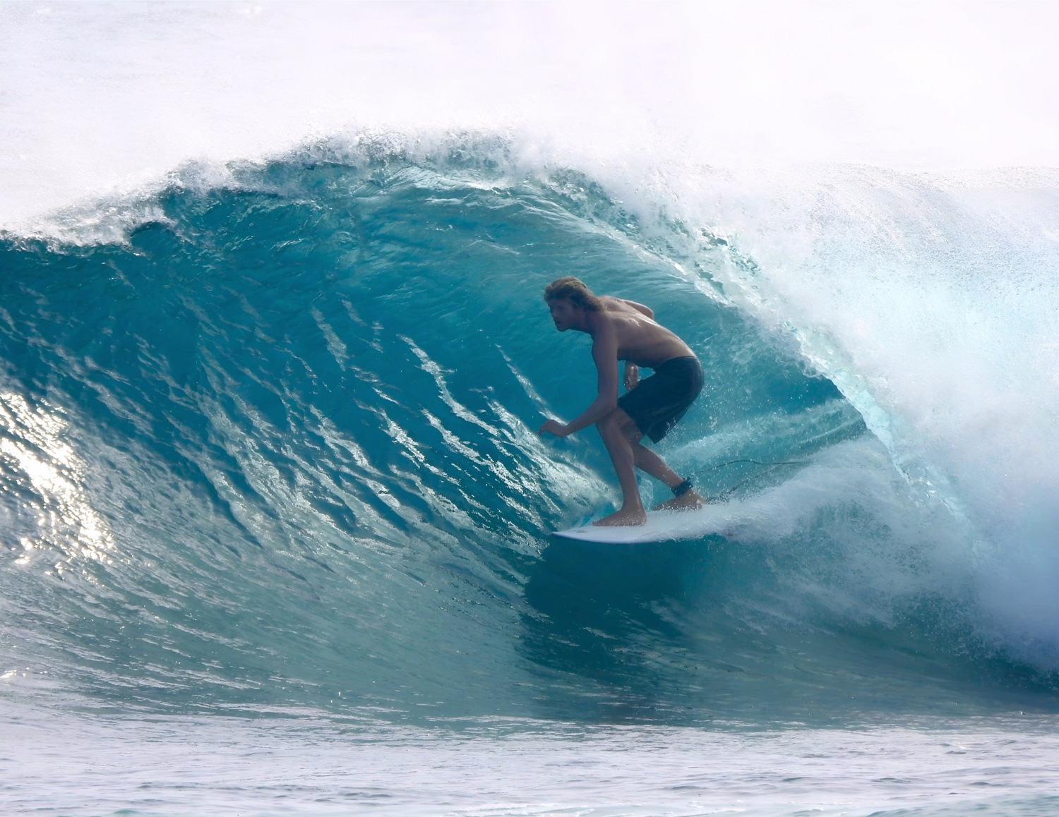 A surfer riding inside a turquoise barrel